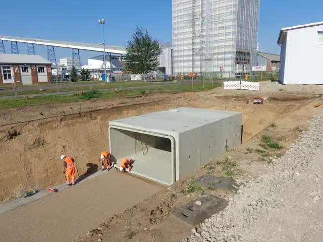 Bauarbeiter bauen einen Betonschacht in einem dafür ausgehobenen Graben ein